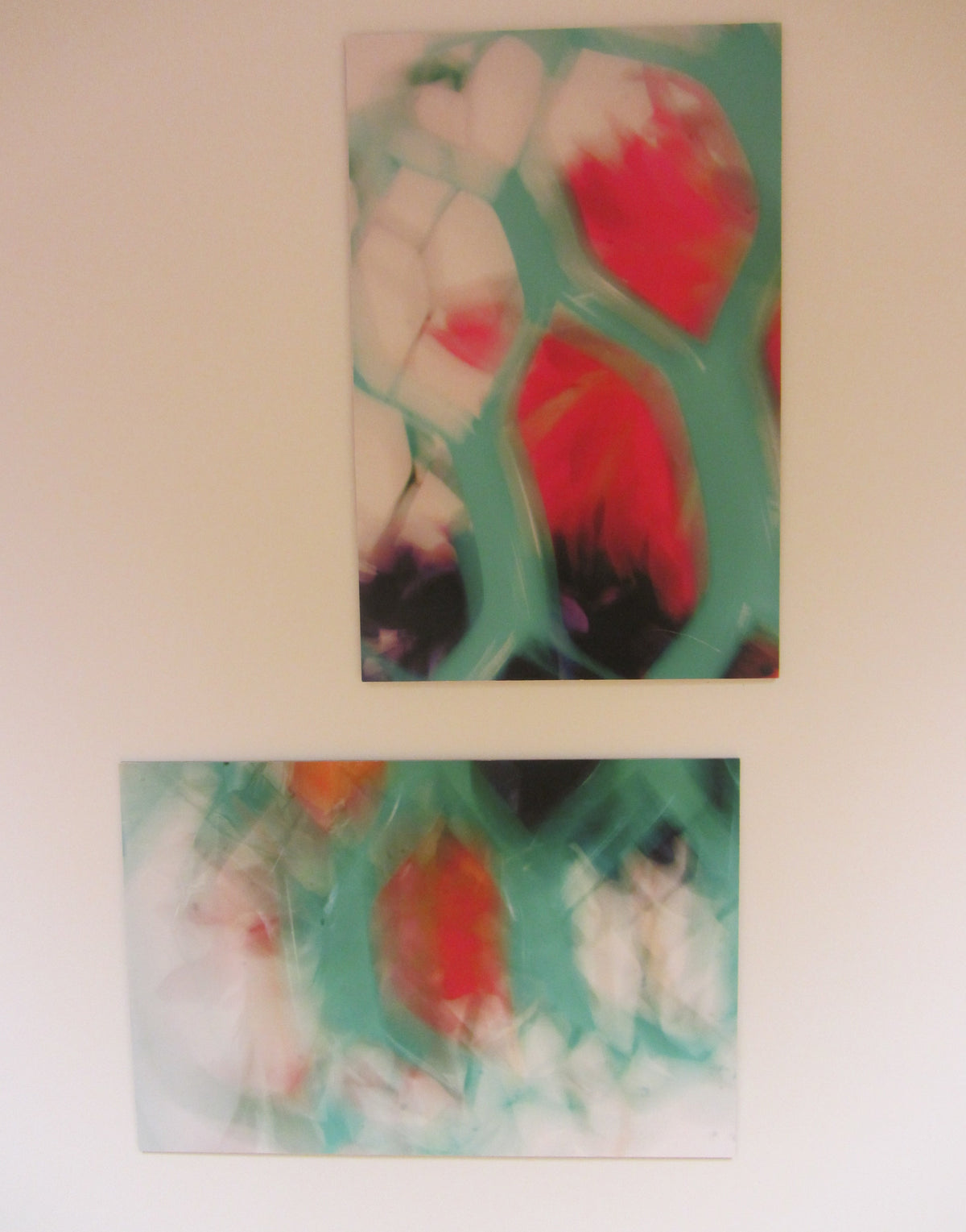 Two abstract rectangular wall art panels hanging vertically on a plain beige wall. The artwork features flowing organic shapes in mint green, white, coral red, and dark navy/black.
